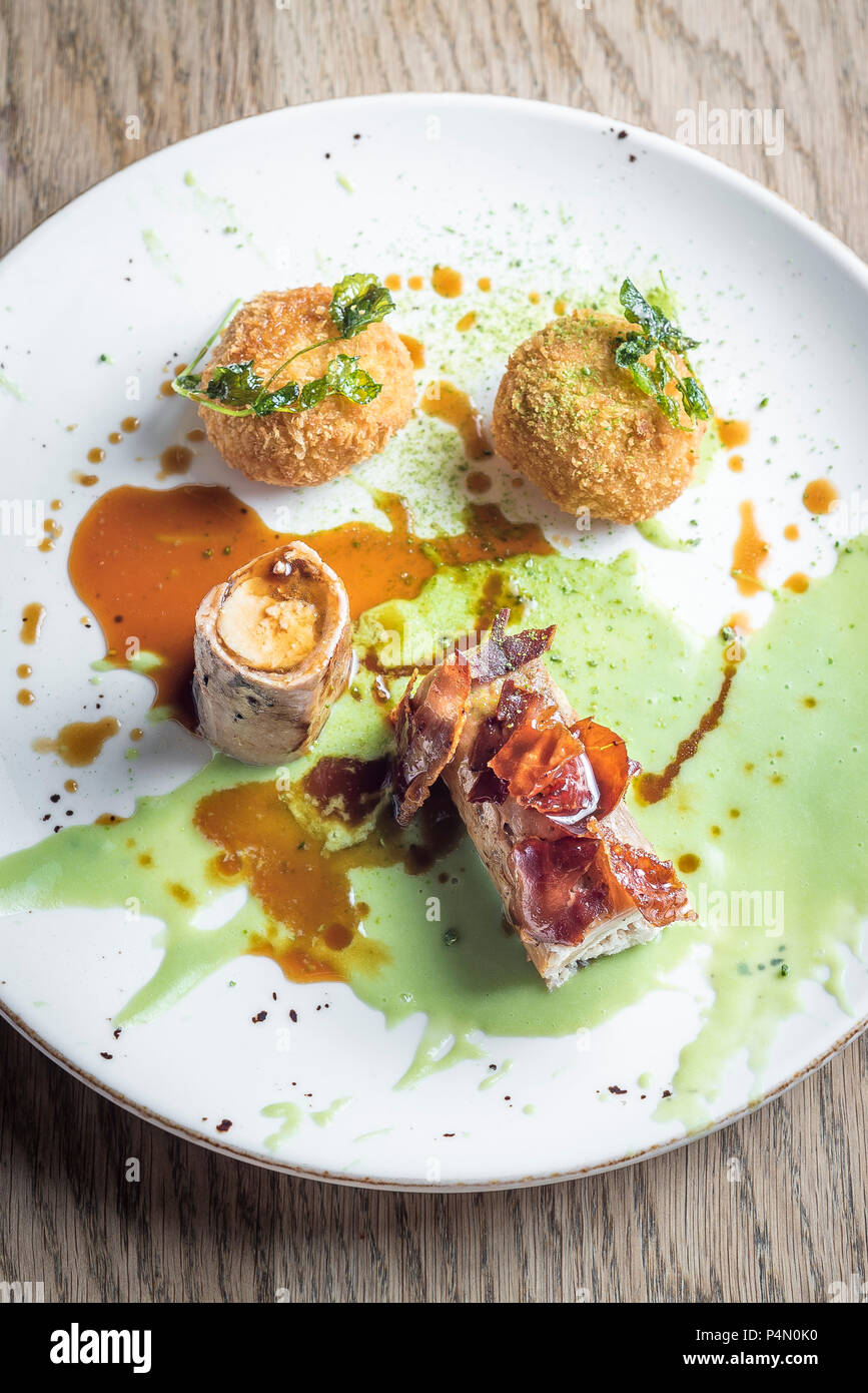 Roasted wild rabbit with crispy bacon and stuffed rice balls arancini and a sweet green pea sauce and gravy Stock Photo