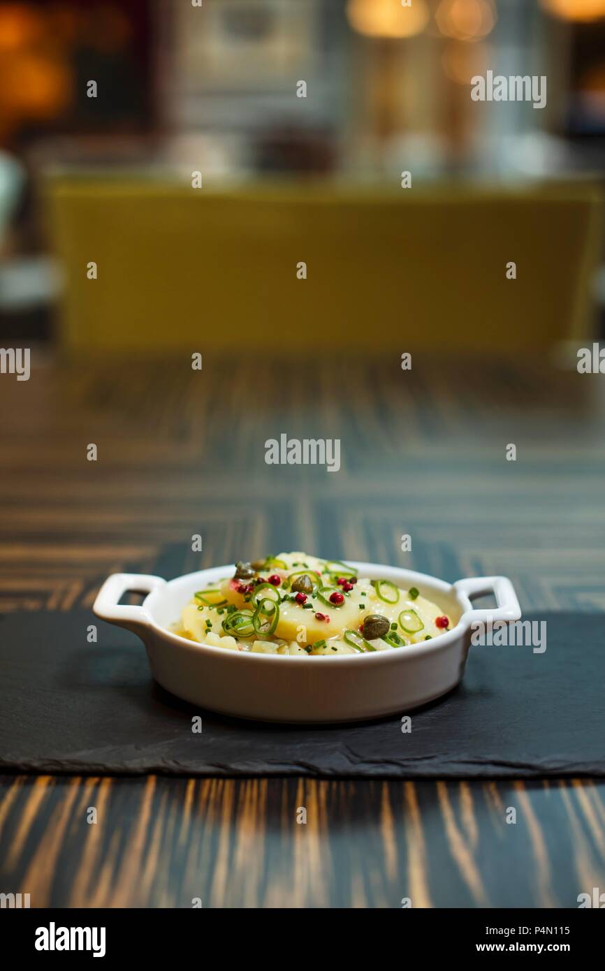 Potato salad with peppercorns and capers in a bowl on a table in a restaurant Stock Photo