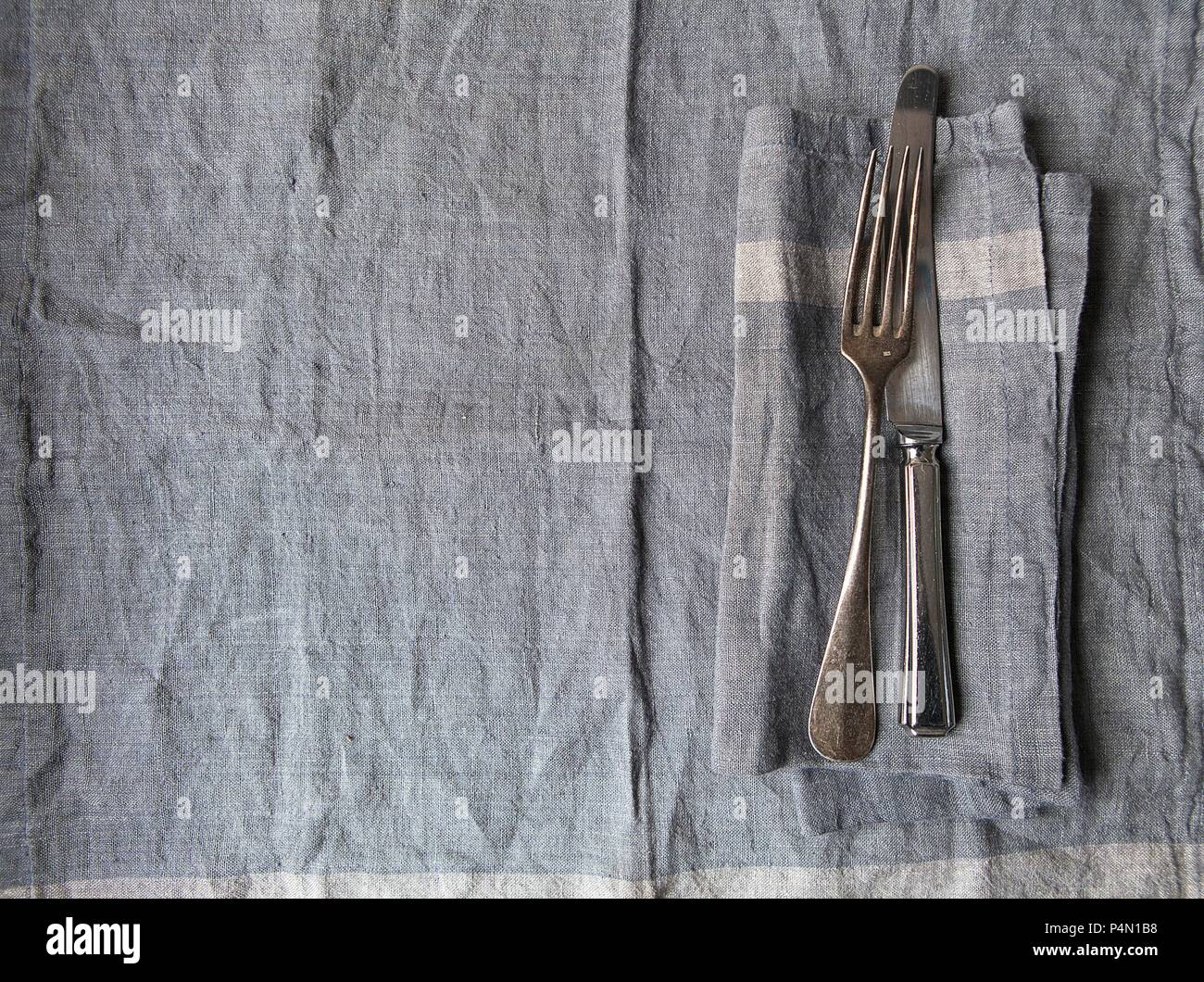 Grey linen place setting with matching grey linen napkin and vintage silver knife and fork Stock Photo