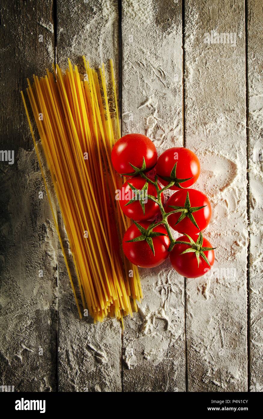 Cherry tomatoes with spaghetti and flour on a wooden table Stock Photo