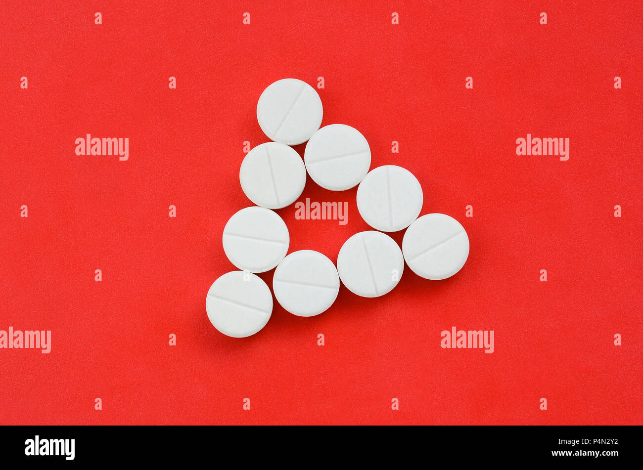Several white tablets lie on a bright red background in the form of an ...