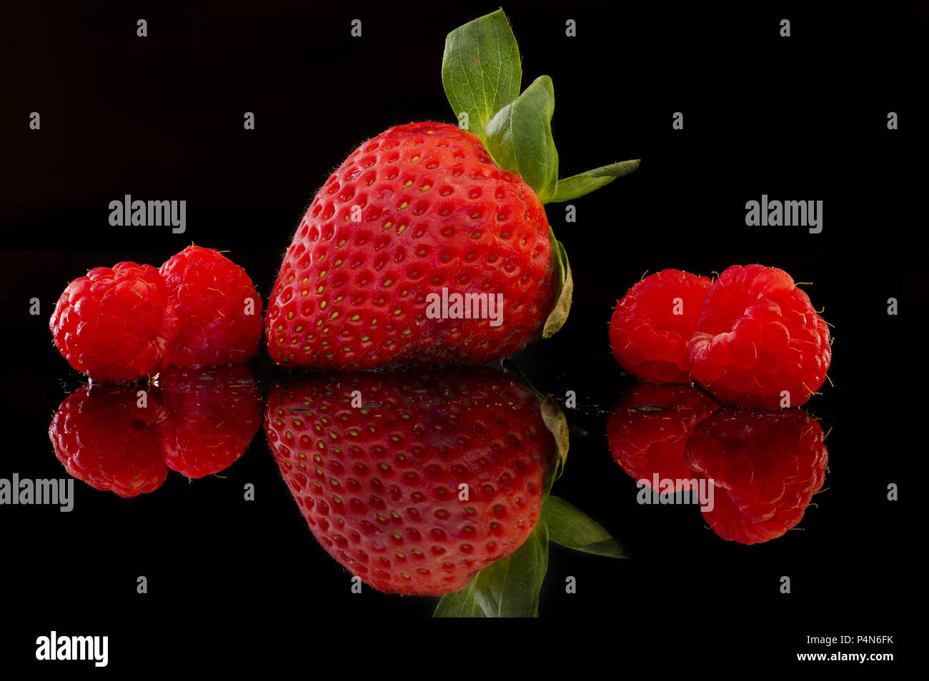 frontal close-up of a large strawberry with four raspberries with ...