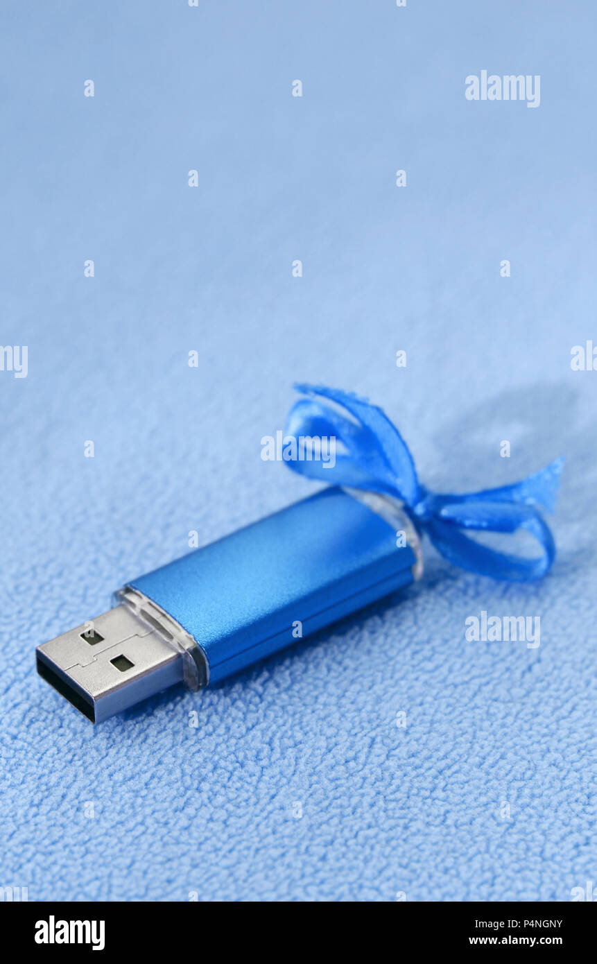 Brilliant blue usb flash memory card with a blue bow lies on a blanket of  soft and furry light blue fleece fabric. Classic female gift design for a me  Stock Photo -