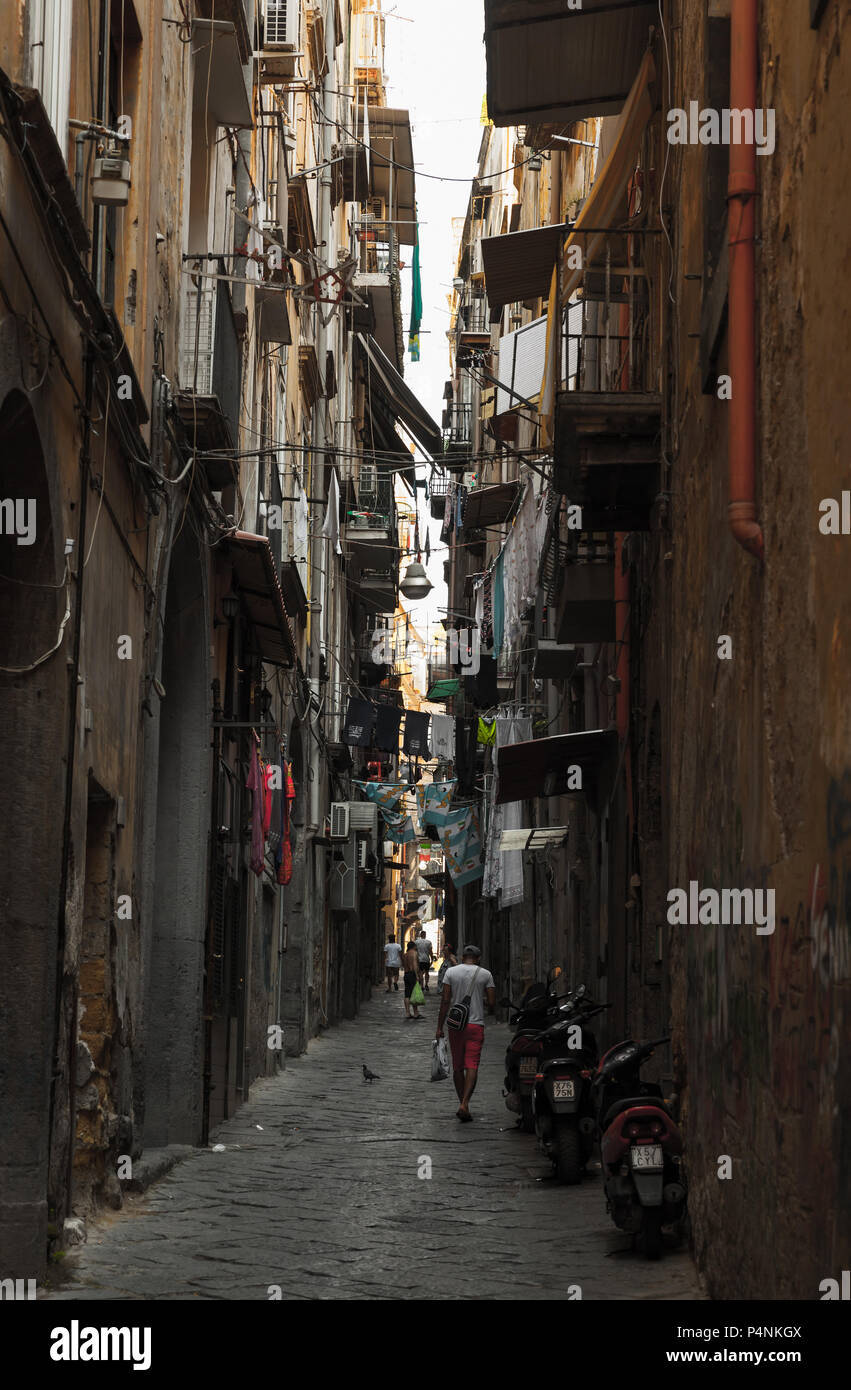 Naples, Italy - August 9, 2015: Ordinary people walk on dark dirty narrow street in old town of Naples Stock Photo