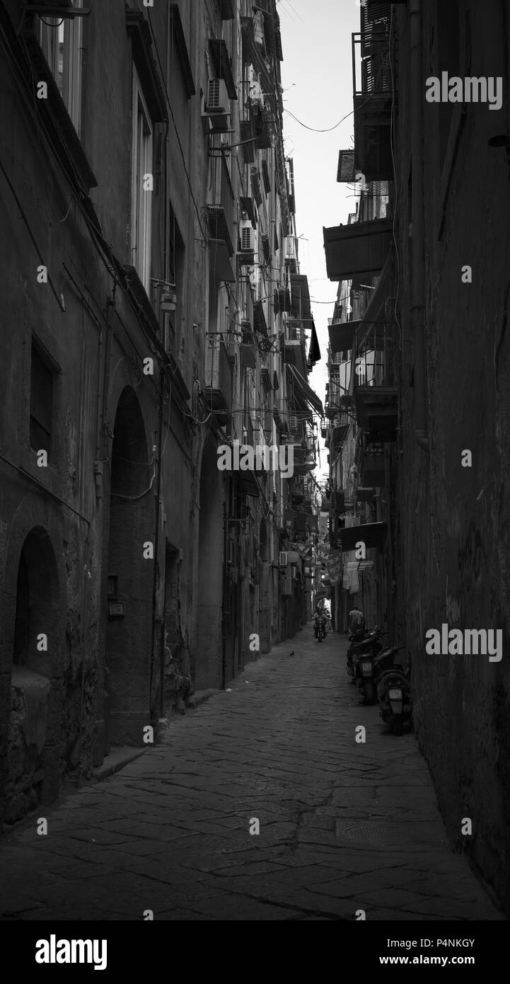 Naples, Italy - August 9, 2015: Black and white photo, ordinary people walk on dark dirty narrow street in old town of Naples Stock Photo