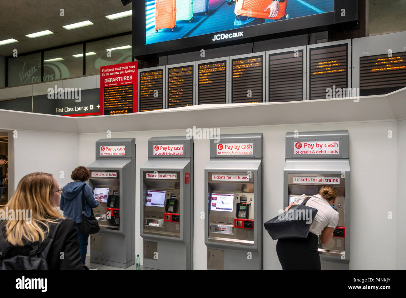 Train passengers at ticket machines under the departures board at