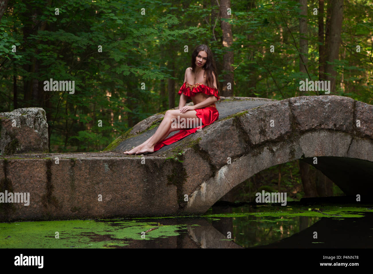 Woman in red dress on bridge in forest Stock Photo