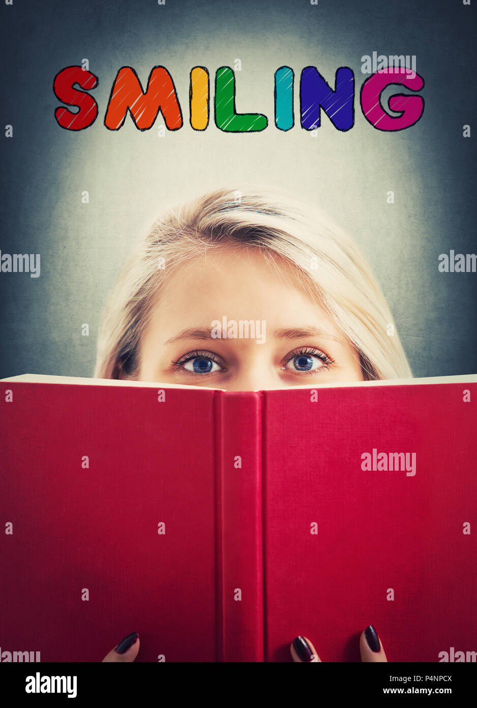 Close up portrait of pretty student girl hiding her personality behind a red opened book like a mask and colorful smiling text inscription above her h Stock Photo