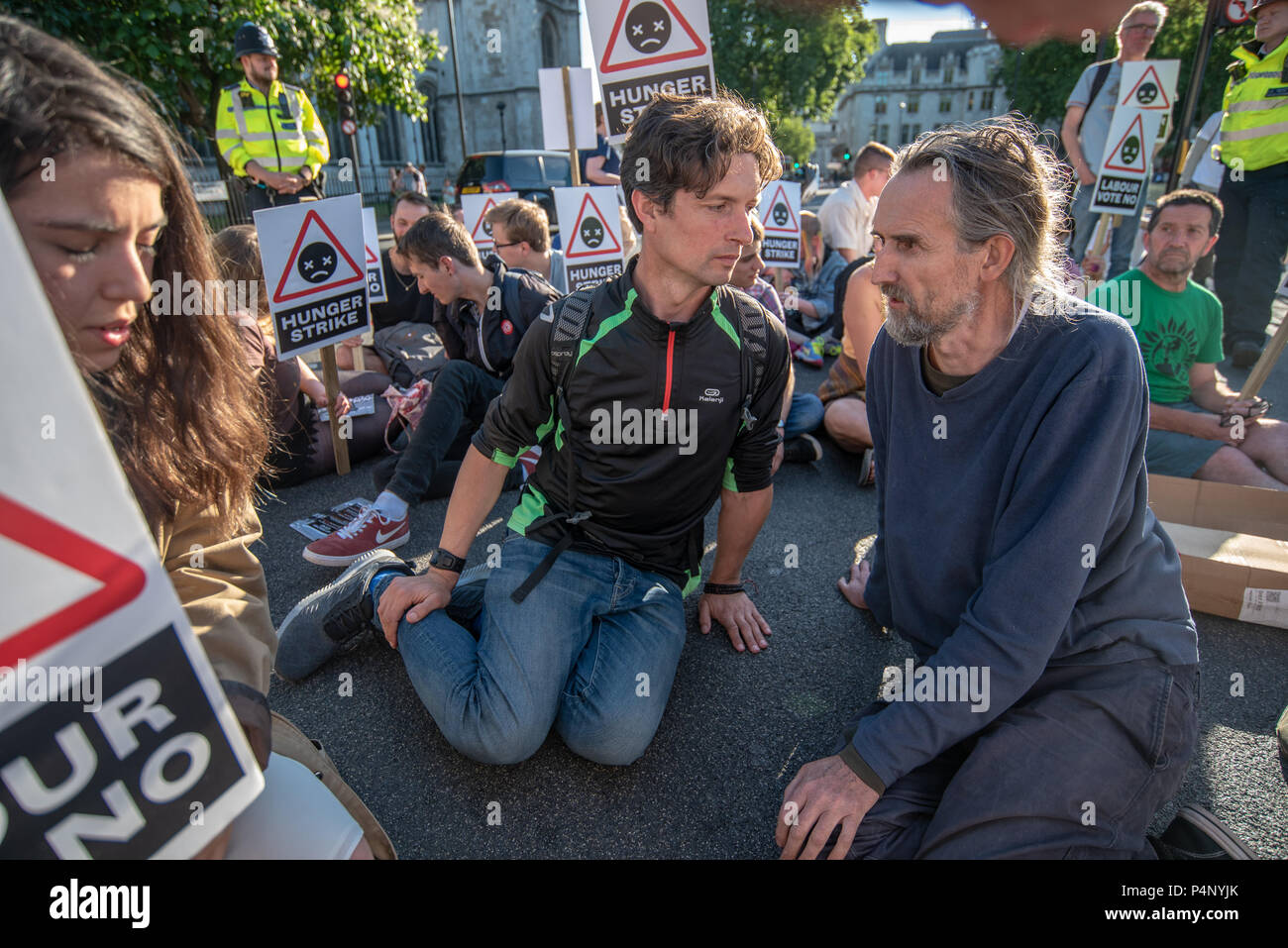 London, UK. 22nd June 2018. Campaigners. including Roger Hallam (right)  against the expansion of Heathrow sit down in the road and block traffic in Parliament Square for 30 minutes holding a banner and placards against Heathrow expansion. Those taking part included some who have been on hunger strike outside the Labour Party HQ for 14 days so far. Police told the protesters individually they risked arrest and removal for obstruction of the highway, but they left after 30 minutes without any arrests. Credit: Peter Marshall/Alamy Live News Stock Photo