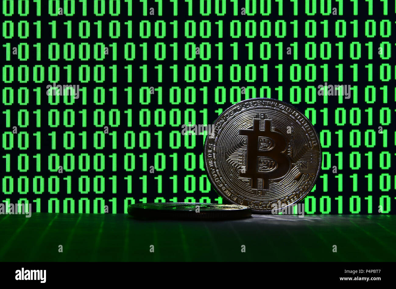 A pair of bitcoins lies on a cardboard surface on the background of a  monitor depicting