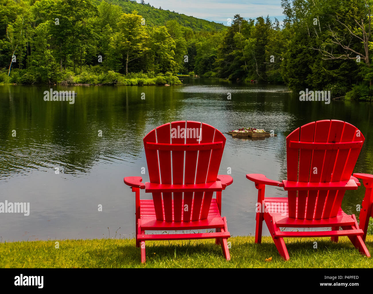 Two Bright Red Adirondack Chairs On The Shoreline Of Lake In