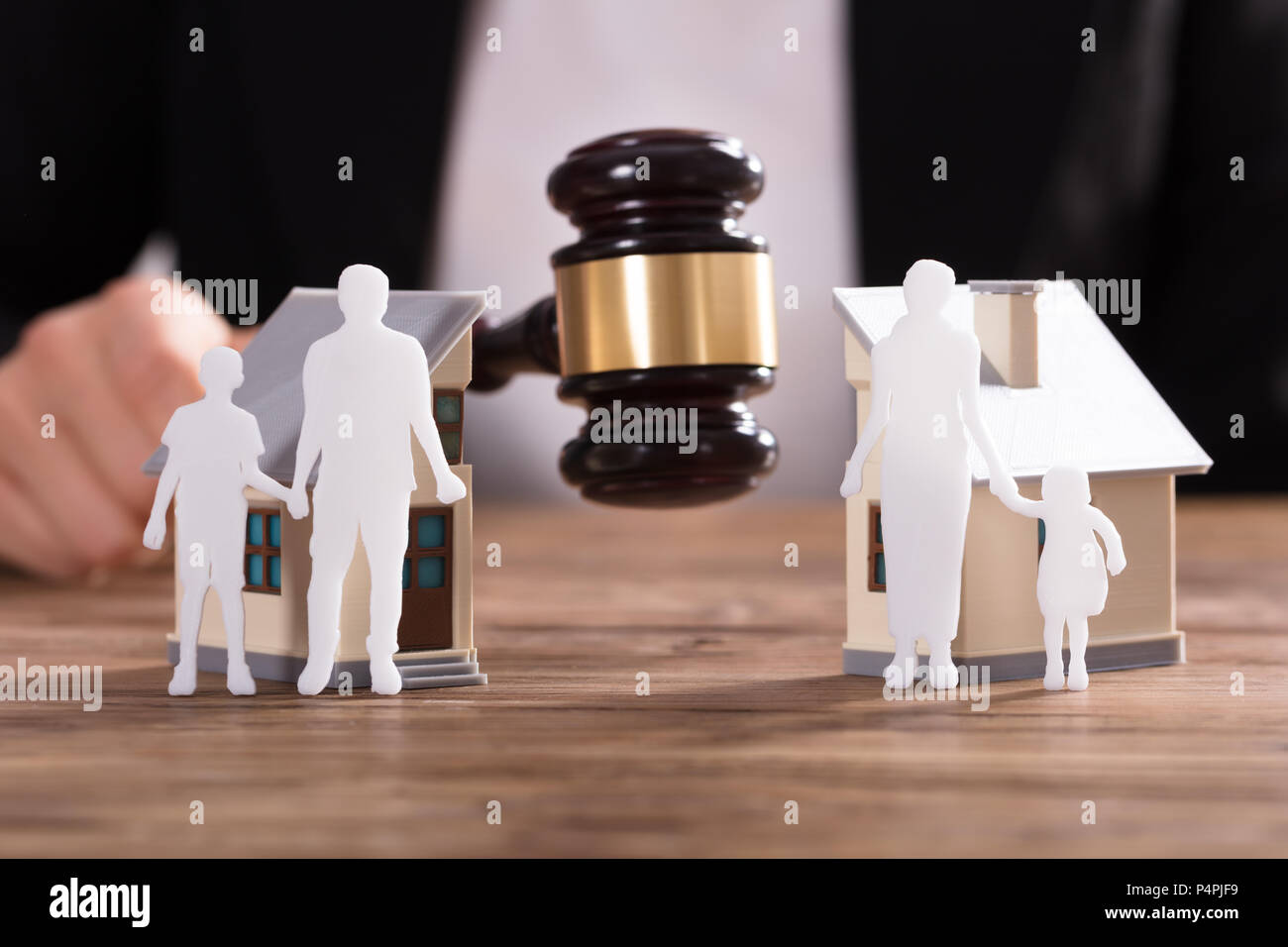 Judge Striking Gavel Between Family Figure Cut Out And Split House Over Wooden Desk Stock Photo
