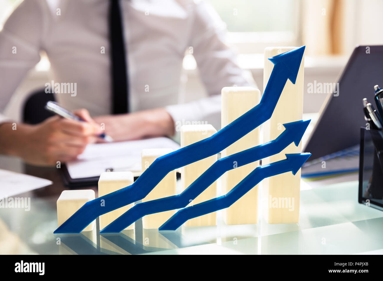 Close-up Of Blue Arrows In Front Of Graph Showing Upward Direction On Desk Stock Photo
