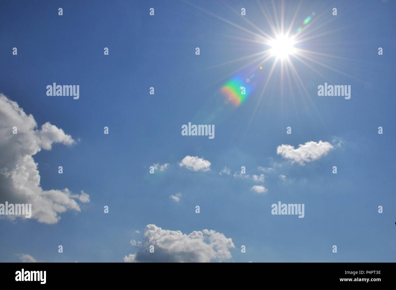 Cloudscape with a blue sky and the sun shining with rainbow reflections Stock Photo