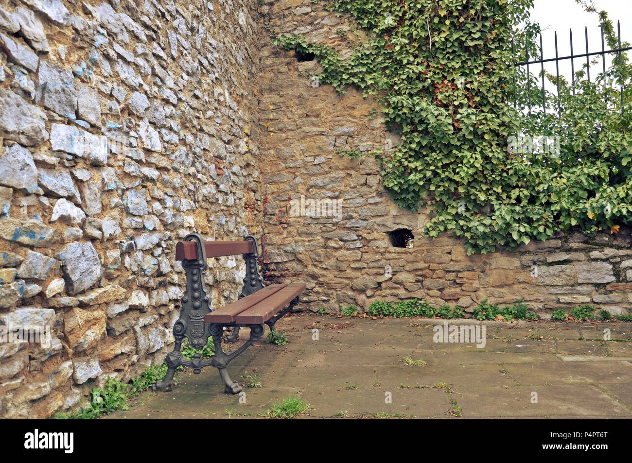Brown wooden bench in a corner of a park with brick wall background, romantic, retro style Stock Photo
