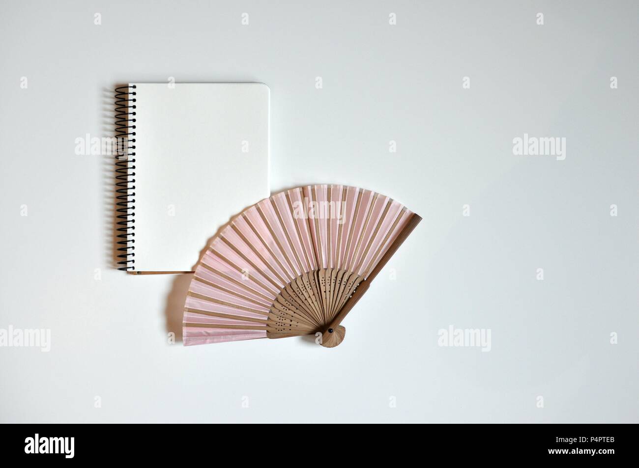 Pink fan and notebook in the middle on white background, flat lay, copy space, minimalist style Stock Photo