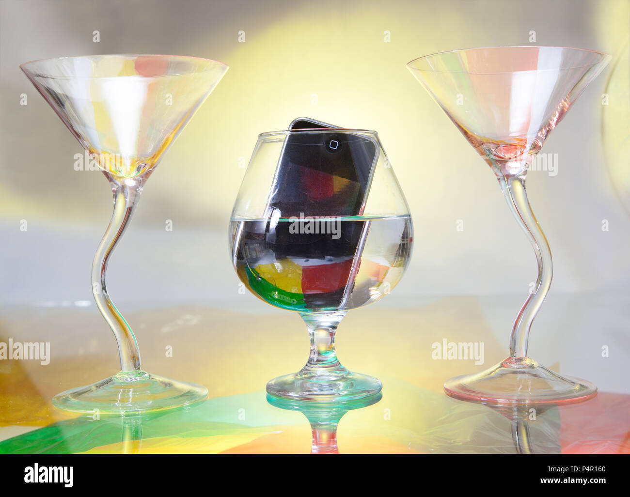 In the middle, you see a brandy glass in which a cell phone is immersed. Two cocktail glasses frame the scene Stock Photo