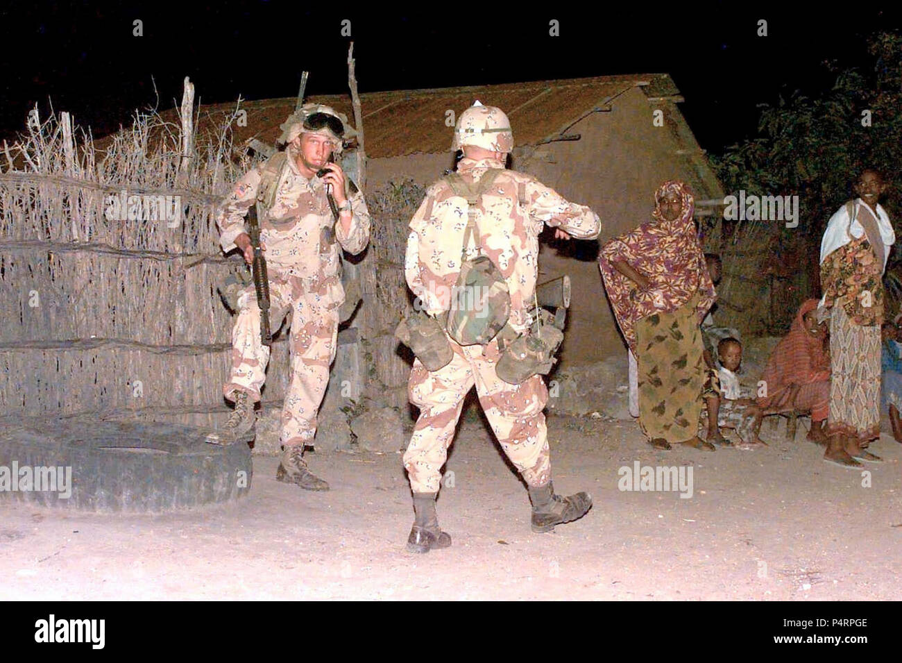 Two US Army troops from the 10th Mountain Division are shown conducting a night time sweep for weapons in the small Somali village of Afgooye.  Some Somali men, women and children are seen at the right.  The 10th Mountain Division from Fort Drum, New York, is deployed to Somalia as part of Operation Restore Hope. Stock Photo