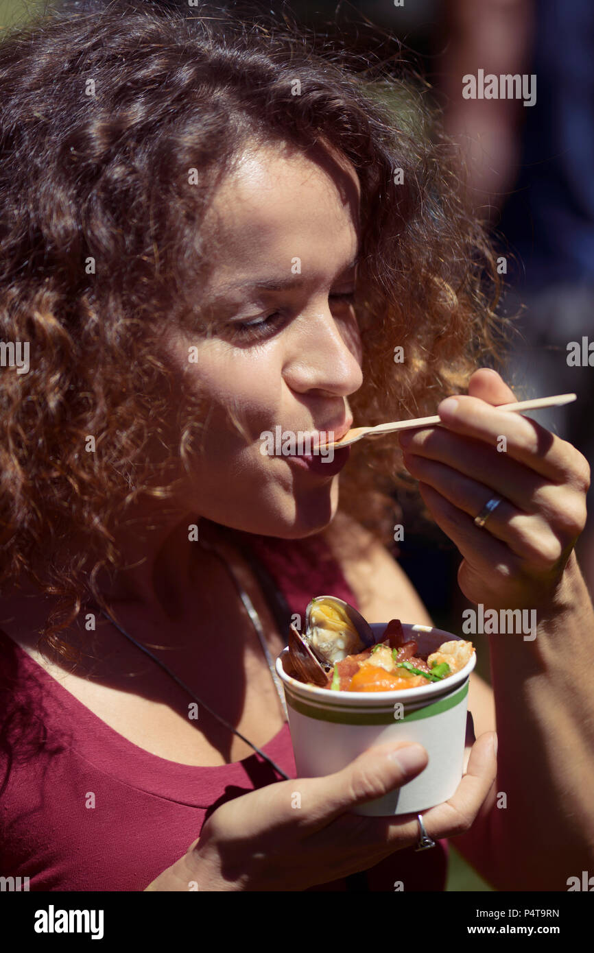 Woman eating street food from a paper cup with enjoyment at the BC seafood festival in Comox, Canada 2018 Stock Photo