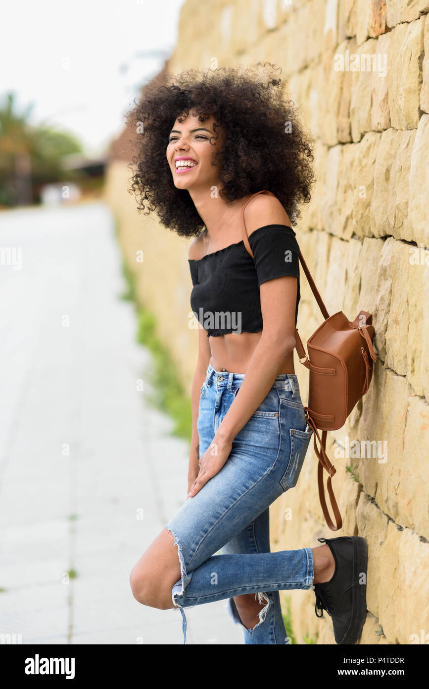 Happy mixed woman with afro hair laughing outdoors. Female wearing ...