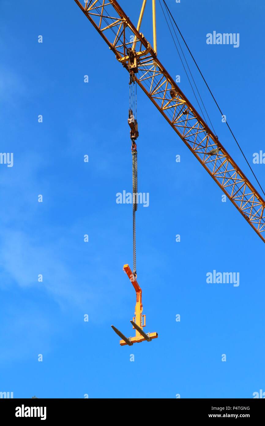 Orange hoisting crane with hanging load on blue sky background. Stock Photo