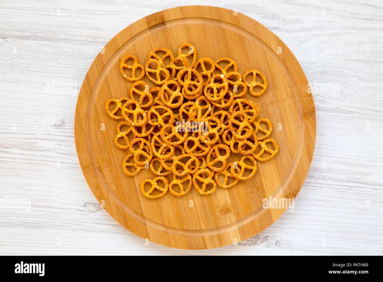 Salt pretzels on round bamboo board on white wooden background, top view. Flat lay Stock Photo