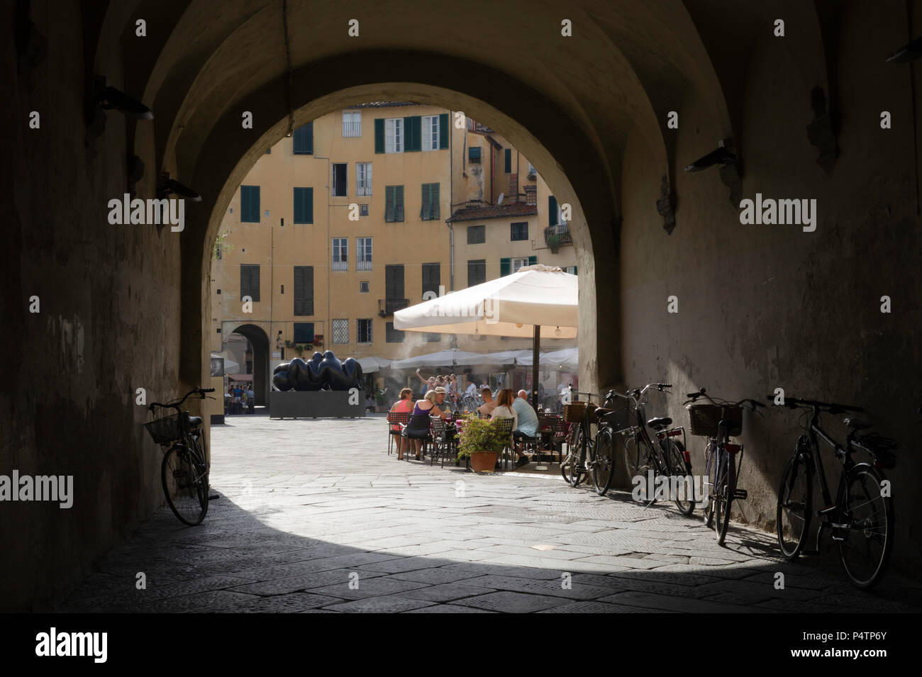A view through one of the entrances into the Antifeatro in Lucca, this view shows diners on the square, and tourists in the background taking a selfie. Stock Photo