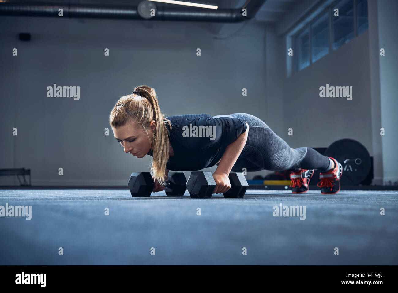 Woman practicing dumbbell push-up exercise at gym Stock Photo