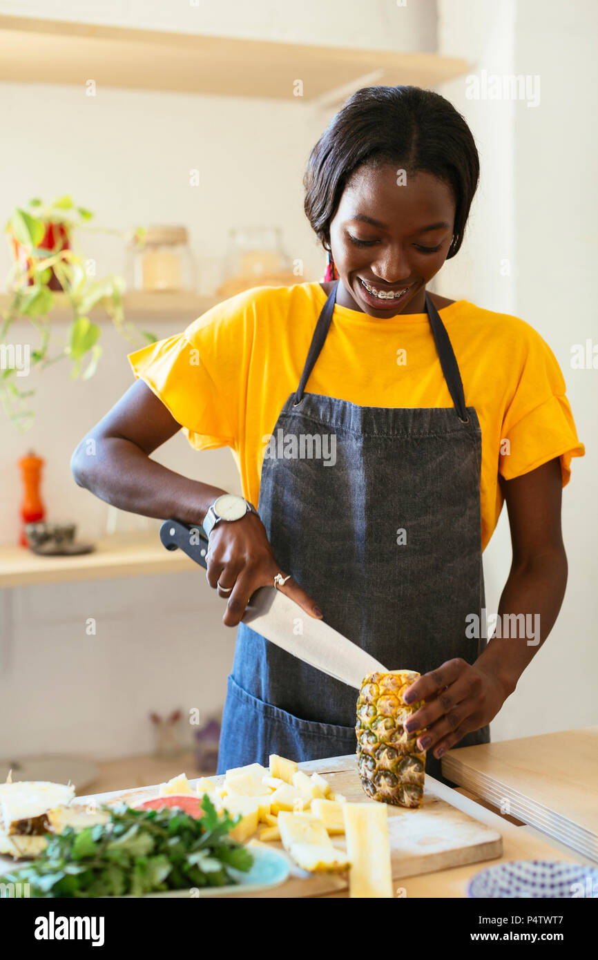 Smiling woman cutting pineapple in kitchen Stock Photo