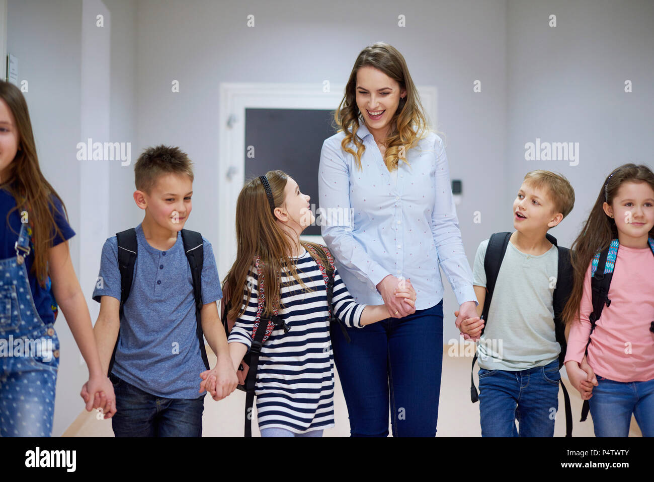Smiling pupils and teacher walking hand in hand on corridor in school Stock Photo
