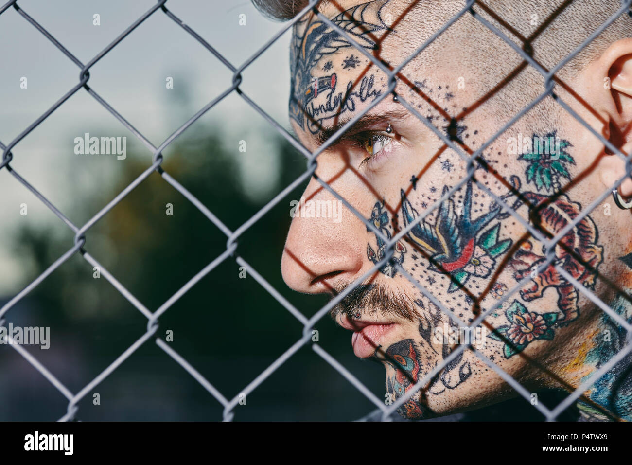 Tattooed face of young man behind fence Stock Photo