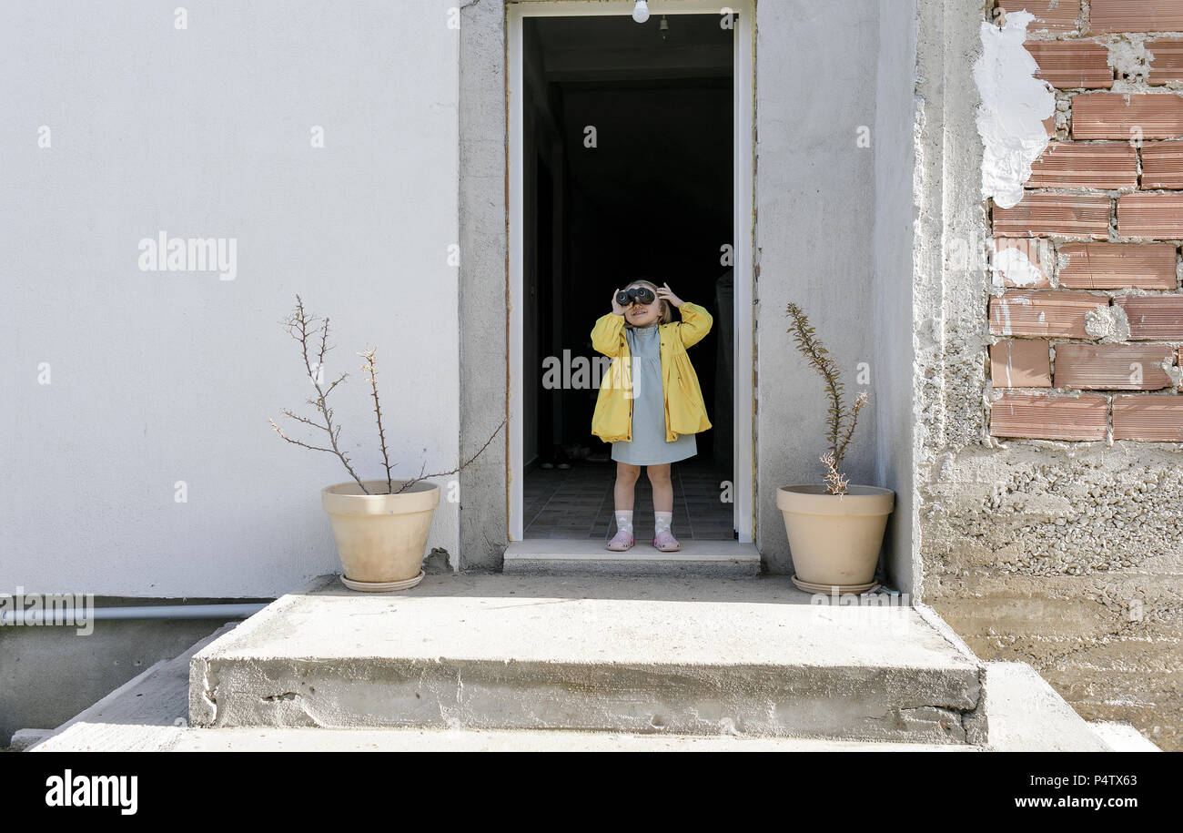 Little girl standing at house entrace using binoculars Stock Photo
