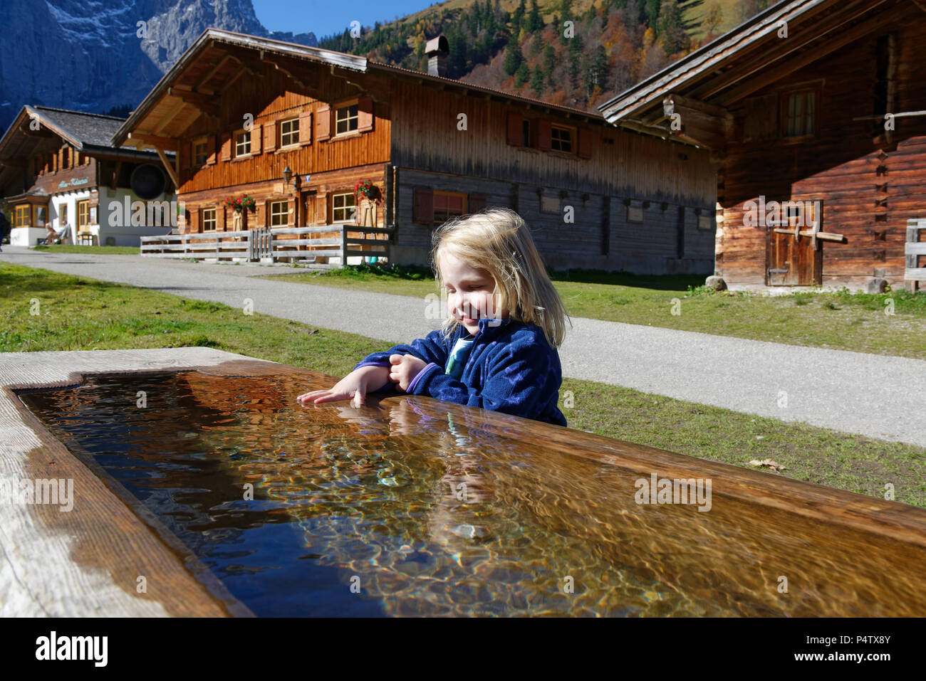 Austria, Tyrol, Eng, small girl bathing hand in drinking trough Stock Photo