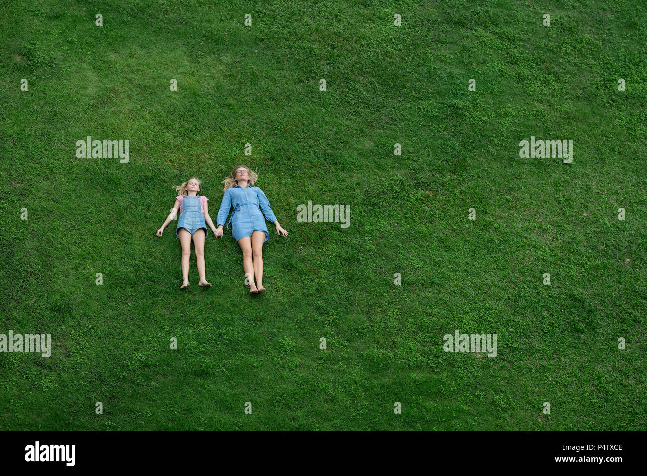 Bird's eye view of mother and daughter lying in garden holding hands Stock Photo
