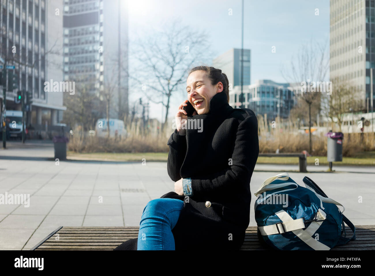 Germany, Essen, laughing young woman on the phone sitting on bench outdoors Stock Photo
