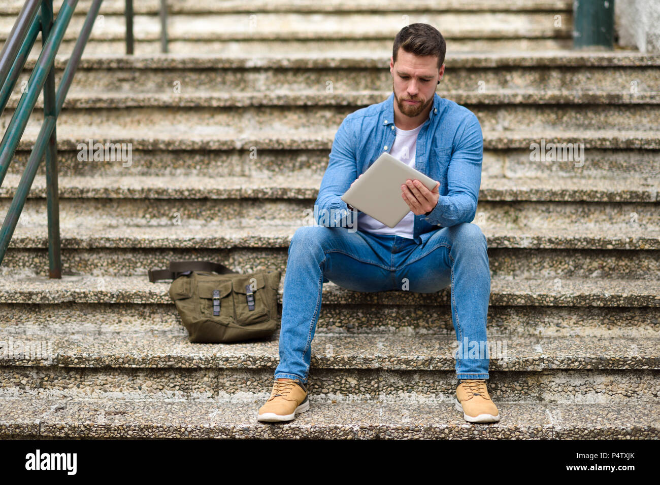 Young man sitting on stairs, working, using digital tablet Stock Photo ...