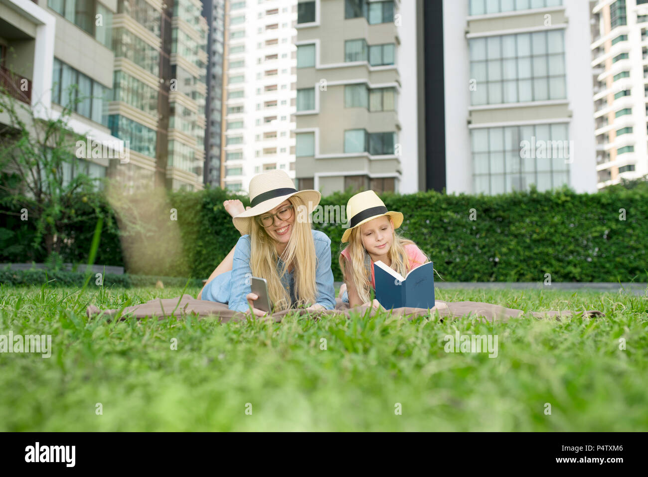 Happy mother and daughter with book and smartphone in urban city garden Stock Photo