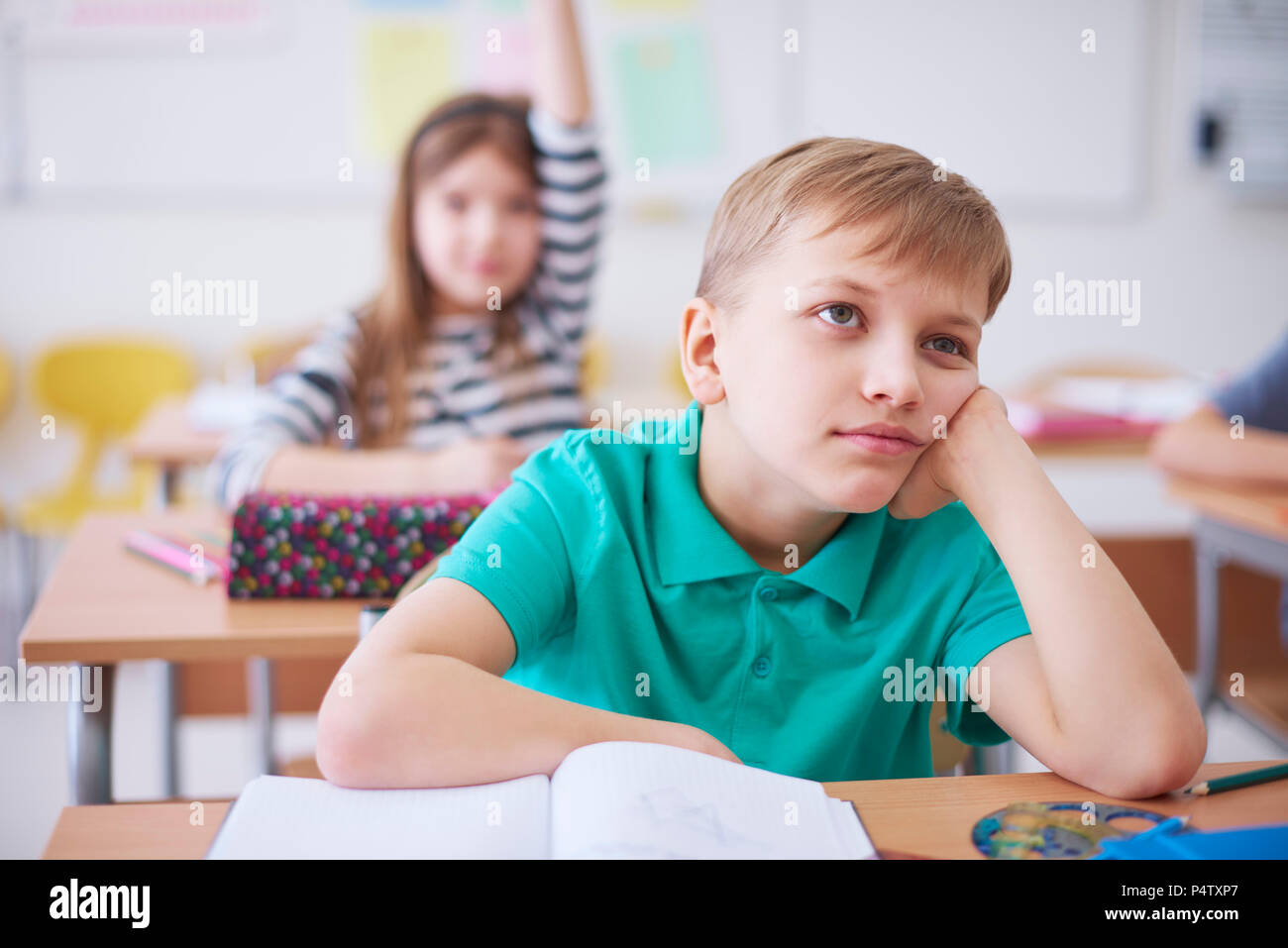 Bored schoolboy in class with girl raising her hand in background Stock Photo