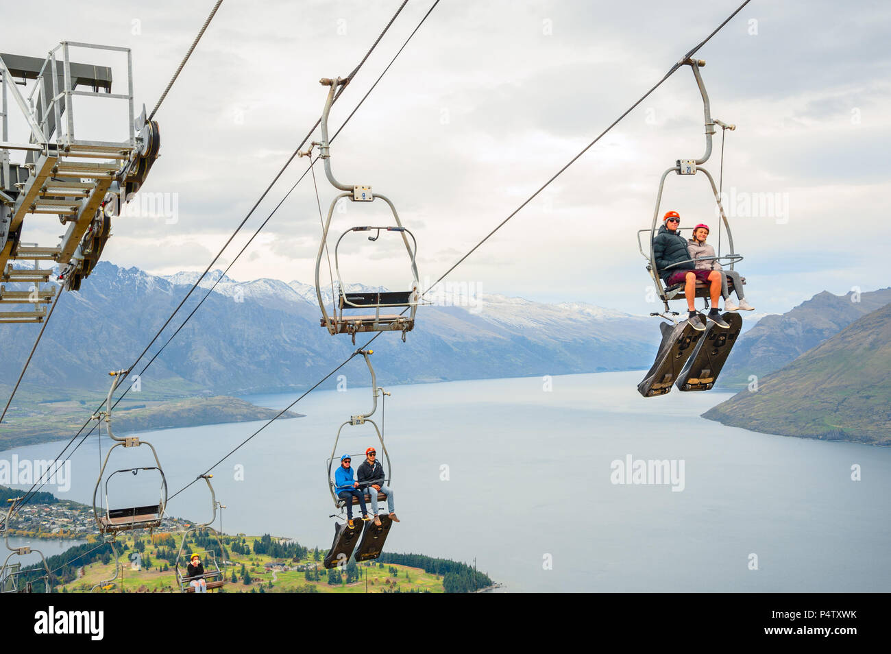 Queenstown, NZ – April 15, 2018: Fun riders with their carts on a cable chair lift going up the hill top for a luge ride with views of Lake and town. Stock Photo