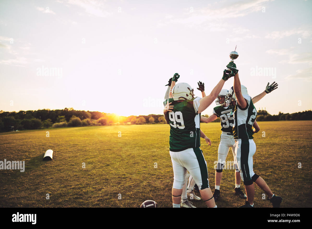 Excited group of American football players standing together in a huddle and raising a championship trophy in celebration Stock Photo