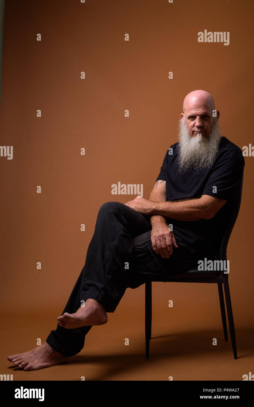 Mature bald man with long gray beard against brown background Stock Photo