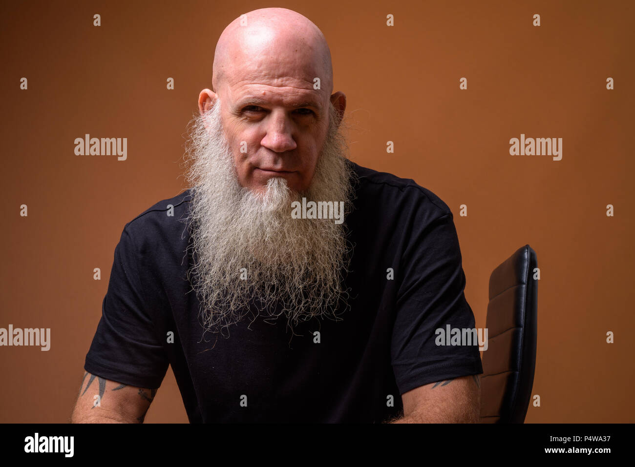 Mature bald man with long gray beard against brown background Stock Photo