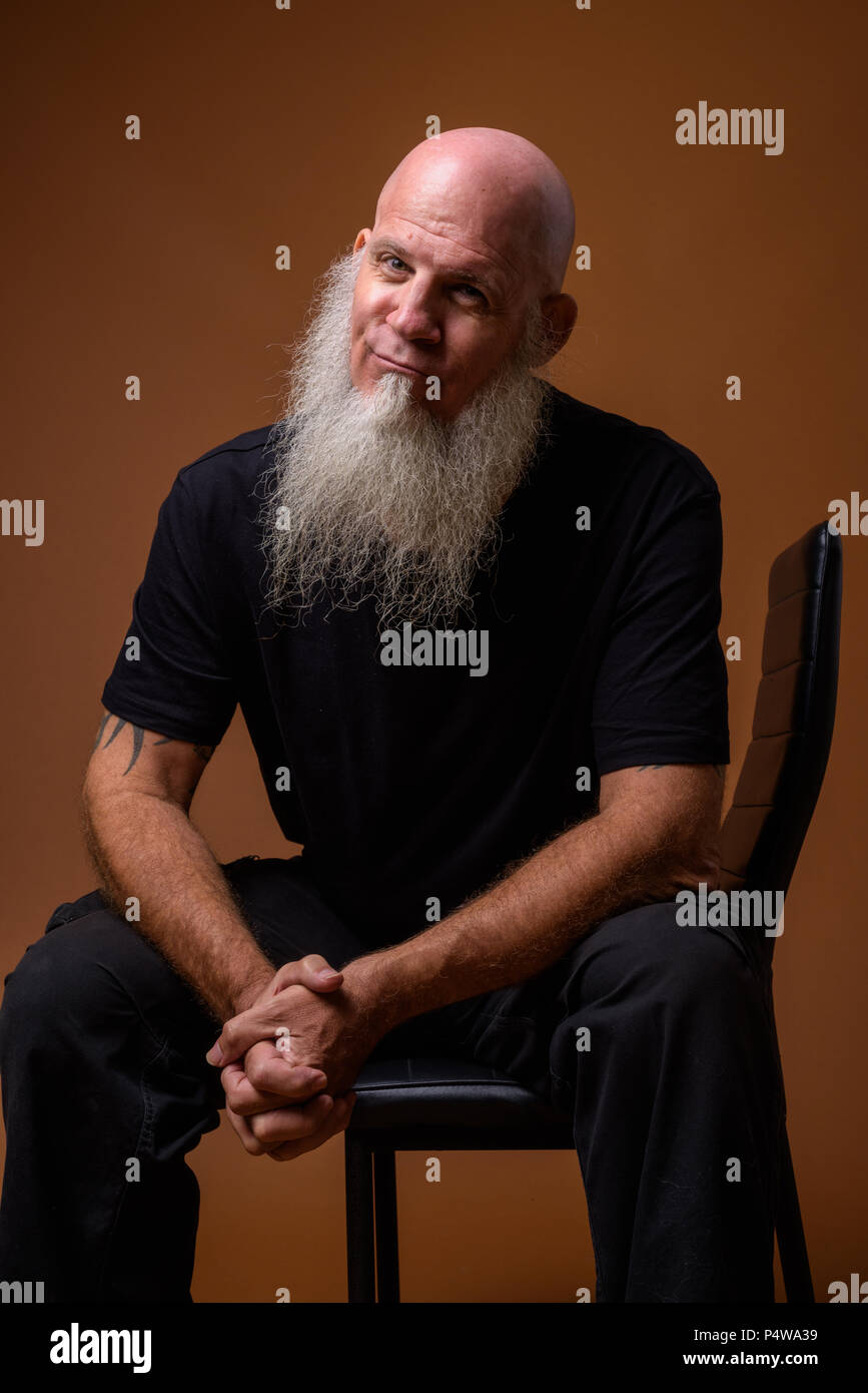 Mature bald man with long gray beard against brown background Stock Photo