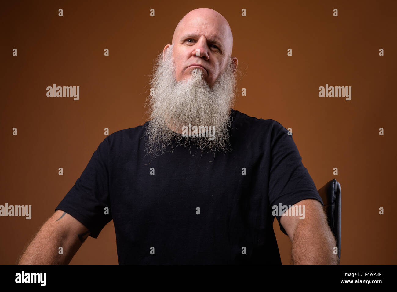 Mature bald man with long gray beard against brown background Stock Photo