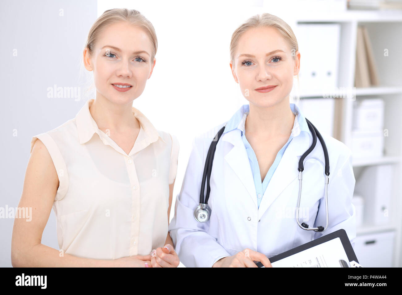 Blonde female doctor and patient talking in hospital office. Health ...