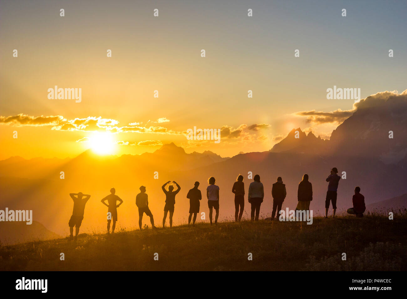 group of people with hands up standing on grass in sunset mountains Stock Photo