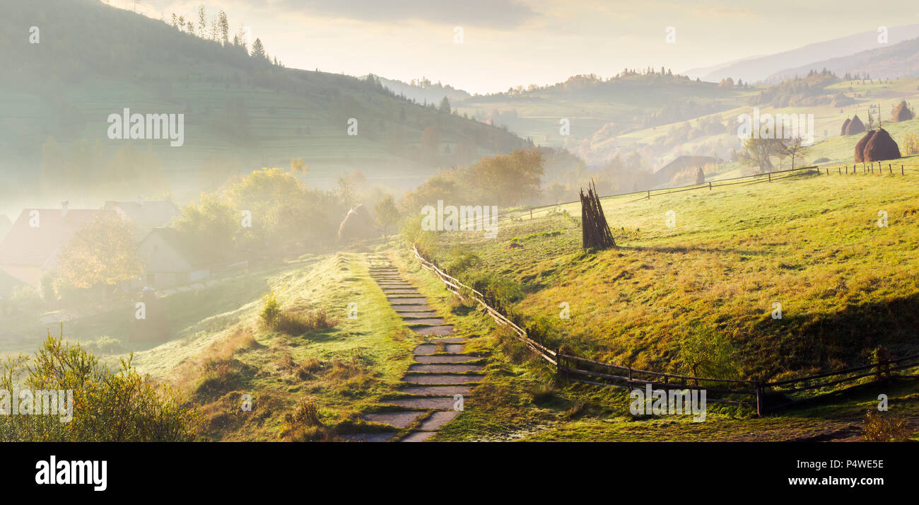 panorama of mountainous rural area on a hazy morning. beautiful landscape of Carpathians. haystacks on the grassy hillside. wooden fence along the foo Stock Photo