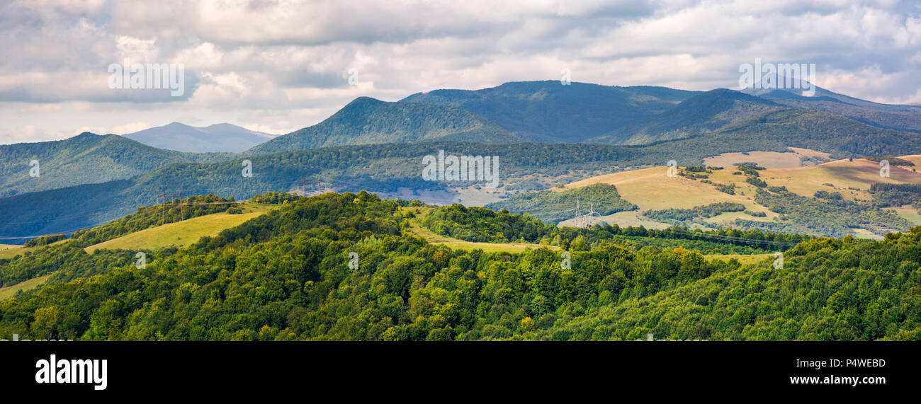 panorama of beautiful Carpathian countryside. power lines run across the nearest hill. Pikui and Gosrta mountains are seen in the distance under the c Stock Photo