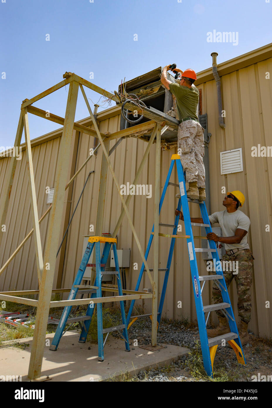 Marine Corps Sgt. Jospeh Spore, a welder with Marine Wing Support Squadron 372, top, prepares an air duct opening for the installation of a new industrial air conditioning unit while Staff Sgt. Hassan Mateyka, an HVAC technician with the 407th Expeditionary Civil Engineer Squadron, secures the ladder May 4, 2017, in Southwest Asia. Expeditionary Marines with MWSS 372 support the Group Special Purpose Marine Air-Ground Task Force-Crisis Response-Central Command, which is collocated with the 470th Air Expeditionary Group. Marines and Airmen frequently partner to sharpen joint skillsets and compl Stock Photo