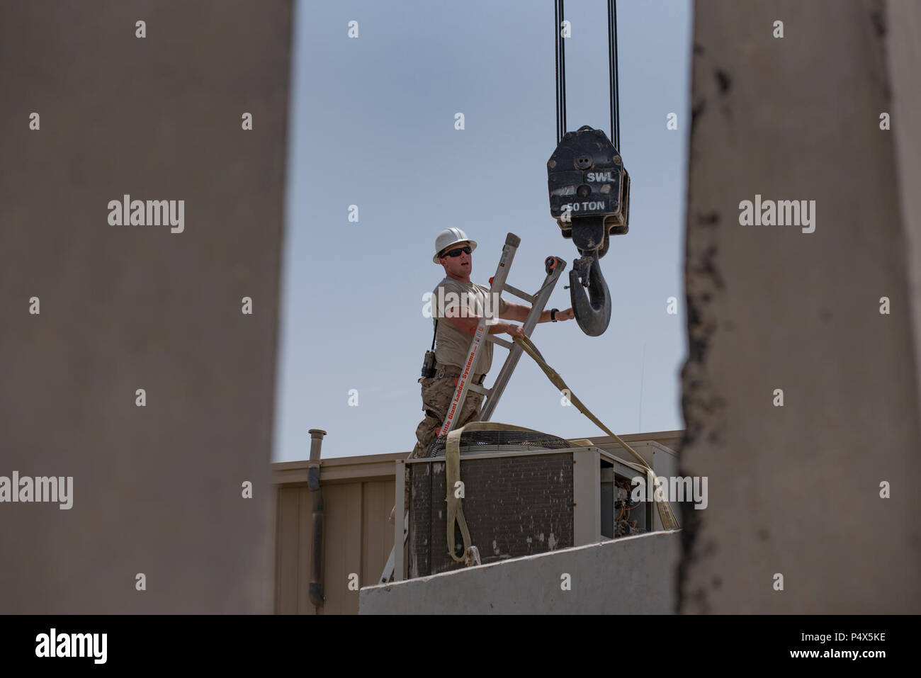 Staff Sgt. Matthew Sayward, a pavement equipment operator with the 407th Expeditionary Civil Engineer Squadron, guides a crane hook into place above a heating, ventilation and air conditioning unit May 4, 2017, in Southwest Asia. Sayward regularly assists HVAC technicians during the move of multi-ton, AC package units on roofs and outdoor mounts. As average daily temperatures in the Air Force Central Command region of operations exceed 100 degrees Fahrenheit, cooling units are essential to support continuous missions of coalition forces against ISIS. Stock Photo